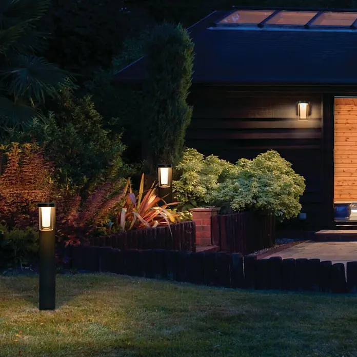 Ledvance Smart+ WiFi LED-Außenwandleuchte CASCADE - Farbe Gehäuse: Dunkelgrau, IP44, 16 x 12 x 18 cm - Eine malerische Gartenszene mit Fokus auf stilvollen Außenleuchten, die eine warme und einladende Atmosphäre schaffen.