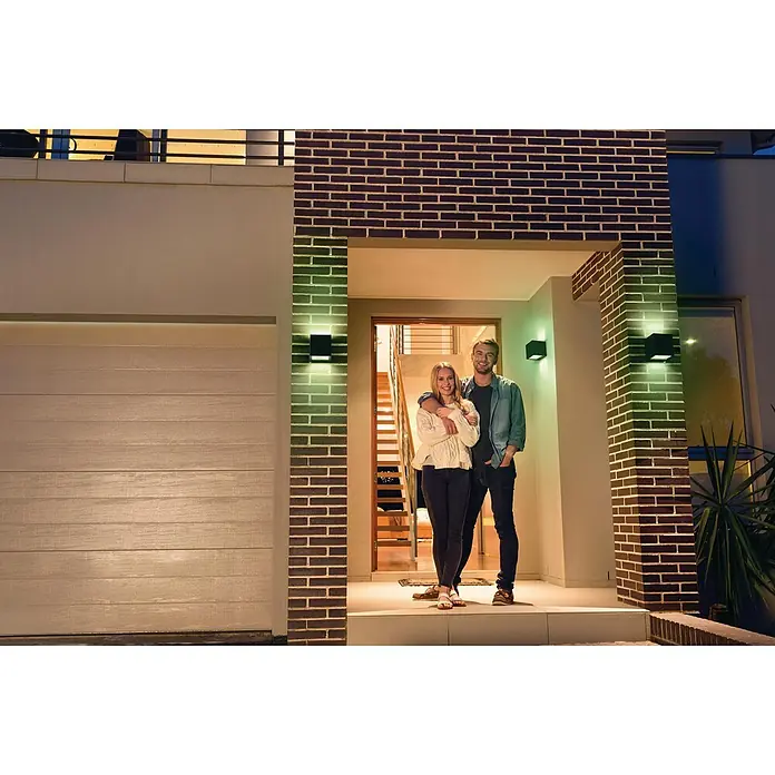 Ledvance Smart+ WiFi LED-Außenwandleuchte BRICKFarbe Gehäuse: Dunkelgrau, IP44 - Ein Paar steht vor einem modernen Haus mit stilvollen Außenleuchten, die die Fassade akzentuieren und für ein einladendes Ambiente sorgen.