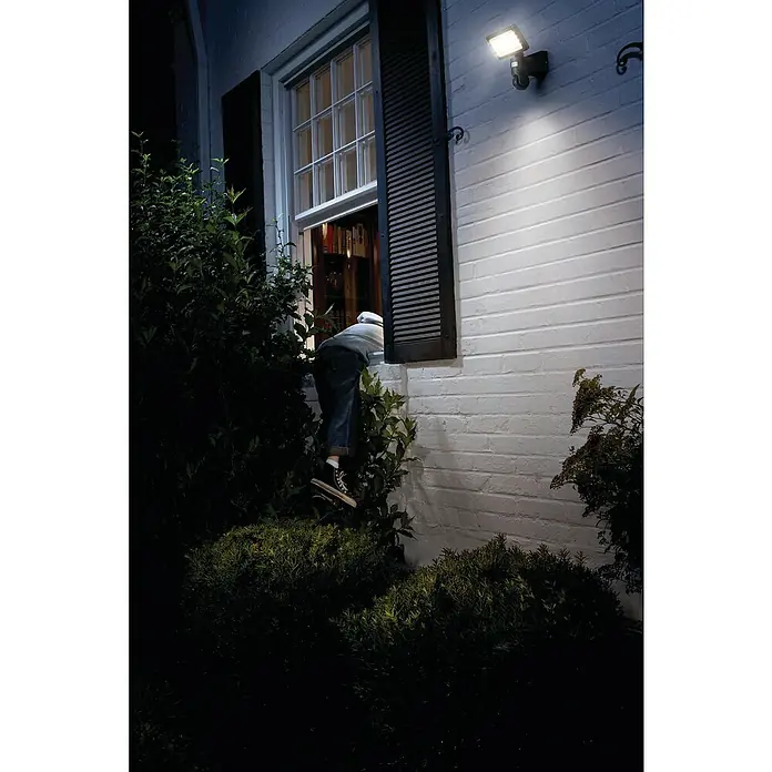 Osram LED-Außenwandleuchte23 W, 20 x 19,7 x 26,2 cm, Dunkelgrau, IP44 - Eine Außenleuchte beleuchtet einen Einbrecher, der in ein Haus durch das Fenster einsteigt. Die helle Lampe sorgt für Sicherheit.