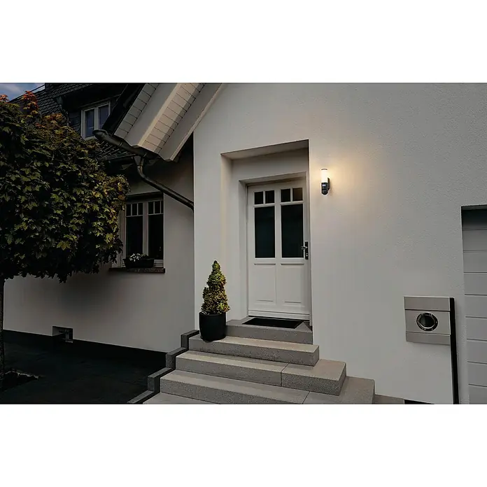 Ledvance Smart+ WiFi LED-Außenwandleuchte - 12 x 8 x 32 cm, Kamera, Dunkelgrau, IP44 - Moderne Außenleuchte neben einer weißen Haustür, die ein warmes, einladendes Licht für Besucher erzeugt und die Fassade betont.