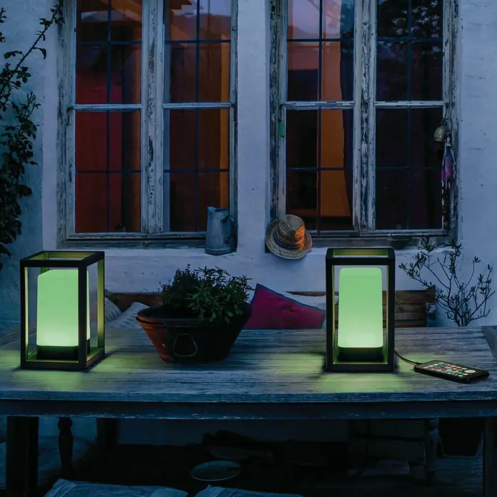 Ledvance Smart+ WiFi Außenlaterne - L x B x H: 12 x 12 x 20,3 cm, Grau, IP44 - Zwei moderne Laternen mit grünem Licht auf einem Tisch im Freien, schaffen eine stimmungsvolle Atmosphäre.