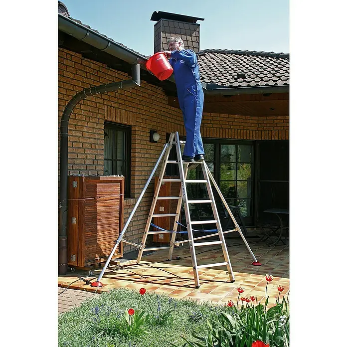Krause Stabilo Doppelleiter - Anzahl Tritte: 14 Stk., Arbeitshöhe: 3,3 m, Aluminium - Mann auf einer Stehleiter, der mit einem roten Eimer Dachrinnen reinigt. Die Leiter ist freistehend und hat Stabilisatoren für sicheren Stand.