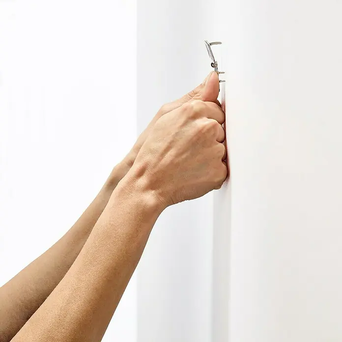 3M Claw Gancho para colgar cuadros - 2 ud., Capacidad de carga: 30 kg - Manos presionando un colgador de cuadros con clavos en una pared blanca para colgar cuadros o decoraciones y embellecer la pared.