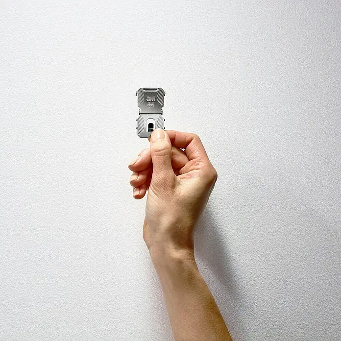 3M Claw Gancho para colgar cuadros - 2 ud., Capacidad de carga: 30 kg - Primer plano de una mano sosteniendo dos tiras adhesivas para colgar cuadros de 3M frente a una pared blanca, perfecto para colgar sin dañar.