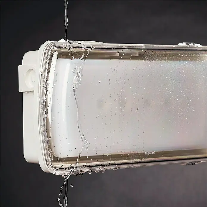 Legrand Tira de luz LED antihumedad IP65 URA21 - Blanco - Primer plano de una luminaria impermeable Legrand salpicada con agua, destacando su capacidad para resistir la humedad.
