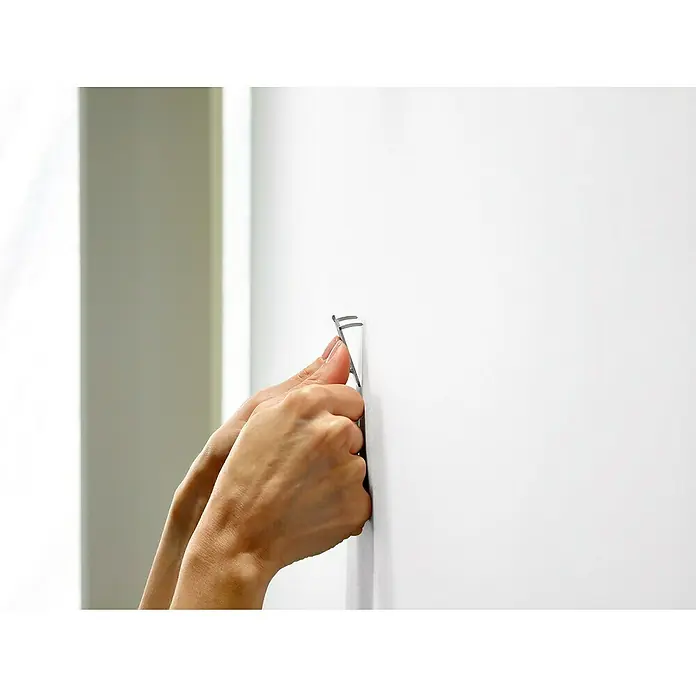3M Claw Gancho para colgar cuadros - 2 ud., Capacidad de carga: 11 kg - Una persona que engancha un colgador de cuadros a una pared blanca para colgar una pintura o una foto. Primer plano de las manos que fijan el gancho.