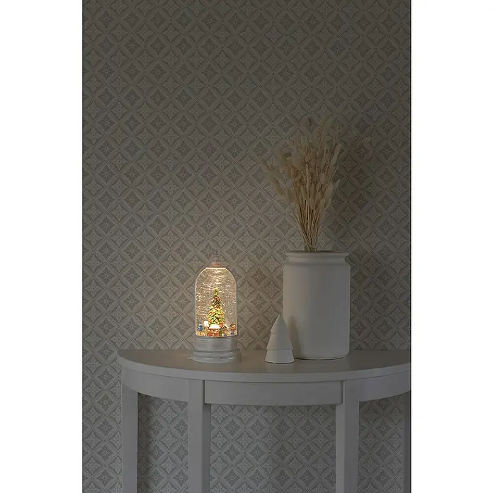 Konstsmide LED-Schneelaterne WeihnachtsmarktInnen, Weiß, 12,5 x 12,5 x 27,2 cm, Batteriebetrieben - Weihnachtliche Szene mit einer bezaubernden Schneekugel, einem dekorativen Keramikbaum und einer eleganten Vase auf einem weißen Tisch.