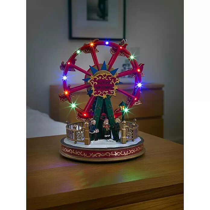 Konstsmide LED-Szenerie Riesenrad - L x B x H: 21 x 21 x 29 cm, Mehrfarbig, Netzbetrieben, LED - Eine festliche Weihnachts-Riesenrad-Dekoration mit roten und goldenen Details, bunten Lichtern und Miniaturfiguren, beleuchtet auf einem Holztisch.