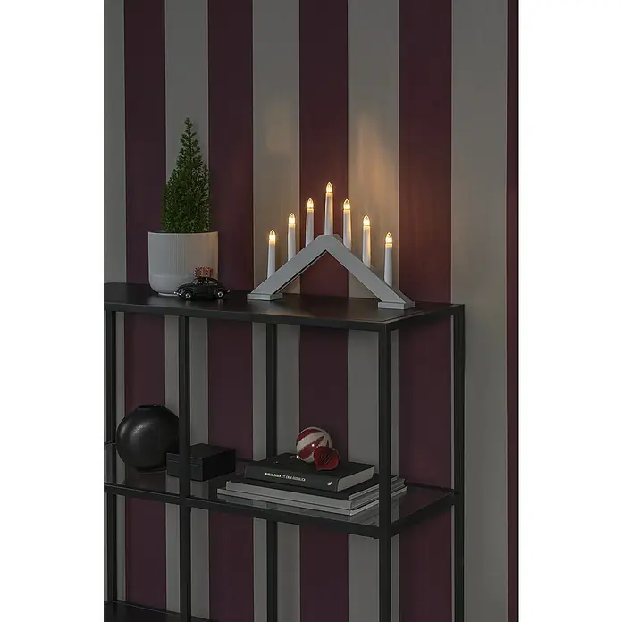 Konstsmide LED-Kerzenständer - Innen, Holz, Höhe: 26,5 cm, Beige - Ein festlicher Lichterbogen mit sieben Kerzen auf einem Regal mit Dekoartikeln vor einer gestreiften Wand.