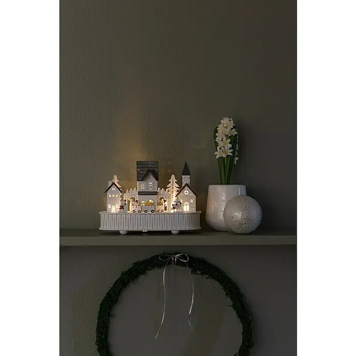 Konstsmide LED-Holzsilhouette - 12 x 22 x 15,5 cm, Weiß, Batteriebetrieben, Warmweiß, 0,3 W - Festliche Dekoration mit einem beleuchteten Weihnachtsdorf, weißen Hyazinthen im Topf und einem glitzernden Dekoball auf einem Regal.