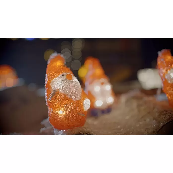 Konstsmide LED-Weihnachtsdekofigur - 7 x 7,5 x 13,5 cm, Rot, Netzbetrieben, LED - Nahaufnahme von beleuchteten orangefarbenen Weihnachtsmännern mit weißen Akzenten in festlicher Umgebung.
