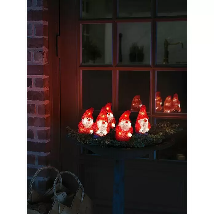Konstsmide LED-Weihnachtsdekofigur - 7 x 7,5 x 13,5 cm, Rot, Netzbetrieben, LED - Fünf beleuchtete Weihnachtsmänner aus durchscheinendem Rot-Weiß auf einer dunklen Schale mit Tannenzweigen im Außenbereich.