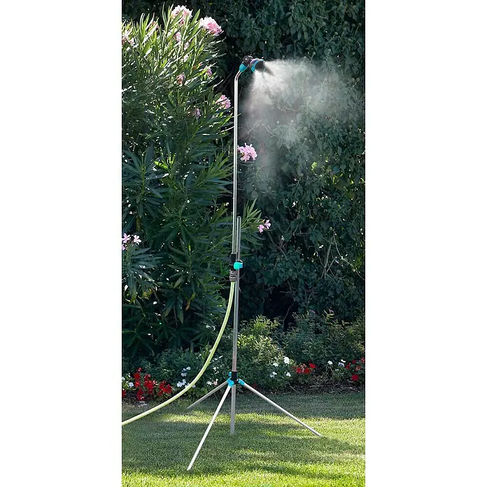 Nebulizador Tripode + Ducha - Ámbito de uso: Jardín, Tipo de conexión: Hembra - Riego: Un aspersor de césped con trípode y manguera está irrigando el césped y las flores circundantes.