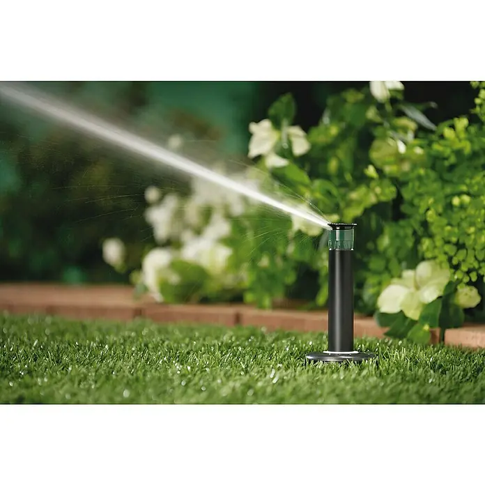 Orbit Aspersor oscilante Regulable - Altura: 10 cm, Polipropileno, Sector de riego por aspersión: 0 ° - 360 ° - Primer plano de un aspersor de césped rociando agua, enclavado en hierba verde con follaje de fondo.