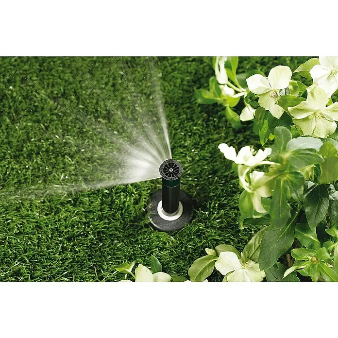Orbit Aspersor oscilante Regulable - Altura: 10 cm, Polipropileno, Sector de riego por aspersión: 0 ° - 360 ° - Sistema de riego en el jardín. Un sistema de aspersores irriga el césped, rodeado de plantas con flores.