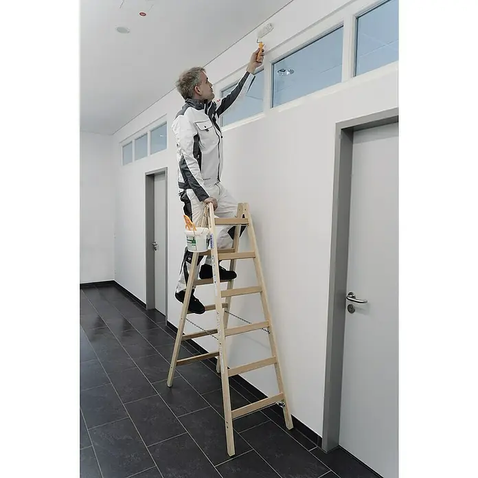 Krause Stabilo Doppelleiter - Anzahl Tritte: 14 Stk., Arbeitshöhe: 3,25 m, Belastbarkeit: 150 kg, Holz - Ein Mann steht auf einer Holzleiter und streicht mit einer Farbwalze die Wand. Er trägt Arbeitskleidung und einen Eimer Farbe.