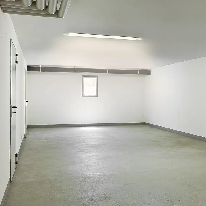 Ritter Leuchten LED-Feuchtraumlichtleiste Slim Pro - L x B x H: 116 x 4,3 x 3,3 cm, Lichtfarbe: Neutralweiß, 36 W, IP65 - Leerer Raum mit Betonboden, weißen Wänden und einer Leuchtstoffröhre. Perfekt als Lagerraum oder zur individuellen Gestaltung geeignet.