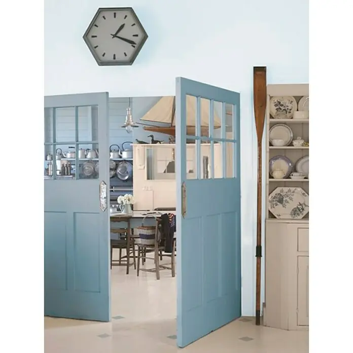 Bruguer Colores del Mundo Pintura para paredes - Mediterráneo azul natural, Mate, 4 l - Vista a través de puertas de cristal pintadas de azul hacia una cocina con decoración náutica y un suelo claro.