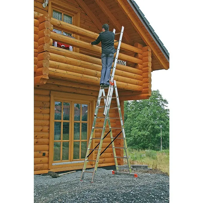 Krause Monto Mehrzweckleiter Tribilo - Arbeitshöhe: 6,85 m, Anzahl Tritte: 27 Stk., Belastbarkeit: 150 kg, Aluminium - Eine Teleskopleiter von KRAUSE steht vor einem Holzhaus, während eine Person auf ihr arbeitet und sichert so einen sicheren Aufstieg.