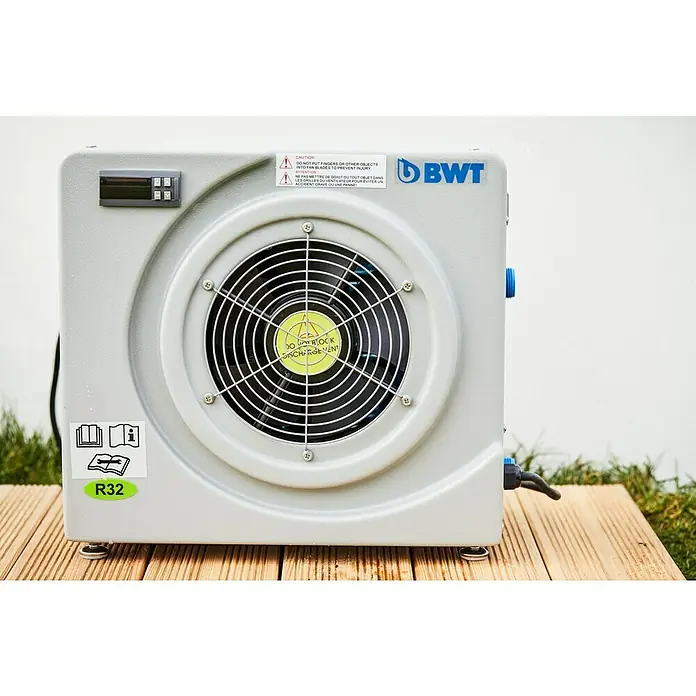 BWT Wärmepumpe Plug & Play 25 - Passend für: Pools bis 25.000 l Beckeninhalt - Nahaufnahme einer BWT-Wärmepumpe auf einer Holzterrasse mit Sicherheitsaufklebern und Bedienfeld.