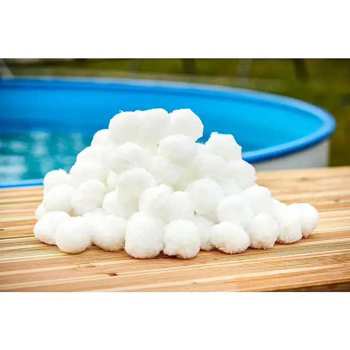 Malibu Filterbälle0,7 kg - Nahaufnahme eines Haufens strahlend weißer Wattebällchen auf einer Holzoberfläche, ideal für Kosmetik oder Bastelarbeiten. Im Hintergrund ist ein Pool zu sehen.