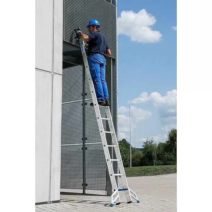 Krause Stabilo Mehrzweckleiter +S - Anzahl Tritte: 36 Stk., Arbeitshöhe: 9,1 m, Aluminium - Aluminiumleiter, die von einem Arbeiter in blauer Uniform mit Schutzhelm verwendet wird, um eine Metallgitterstruktur mit einem Bohrer zu erreichen.