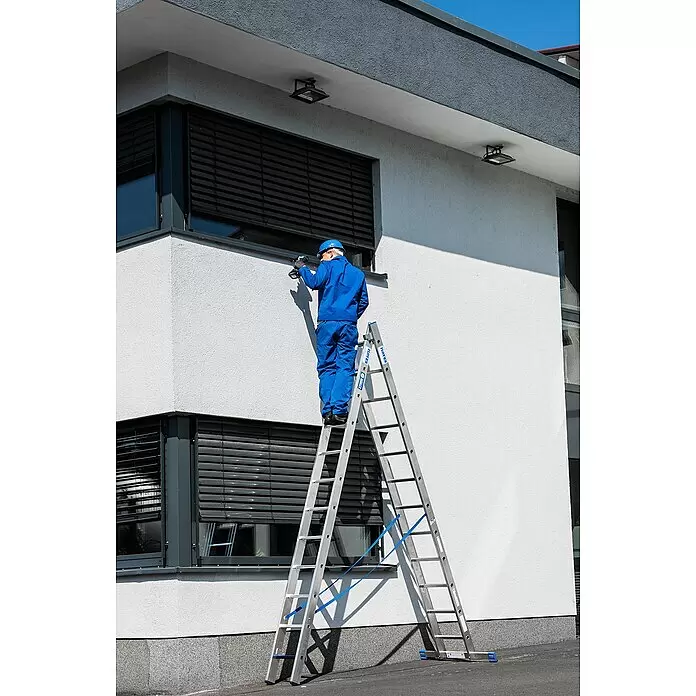 Krause Stabilo Mehrzweckleiter +S - Anzahl Tritte: 24 Stk., Arbeitshöhe: 6,7 m, Aluminium - Arbeiter in blauem Overall auf einer silbernen Aluminiumleiter mit blauen Stabilisierungsgurten, der Arbeiten an einer Gebäudewand ausführt.
