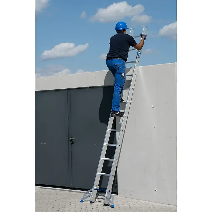 Krause Stabilo Schiebeleiter +S - Anzahl Tritte: 24 Stk., Arbeitshöhe: 6,7 m, Aluminium - Ein Mann mit Schutzhelm klettert auf einer silbernen Aluminiumleiter an einer Betonwand hoch, um Reparaturen durchzuführen.