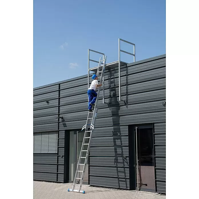 Krause Stabilo Schiebeleiter +S - Anzahl Tritte: 24 Stk., Arbeitshöhe: 6,7 m, Aluminium - Mann in blauer Arbeitskleidung steigt eine silberne KRAUSE Leiter auf eine Gebäudedachplattform.