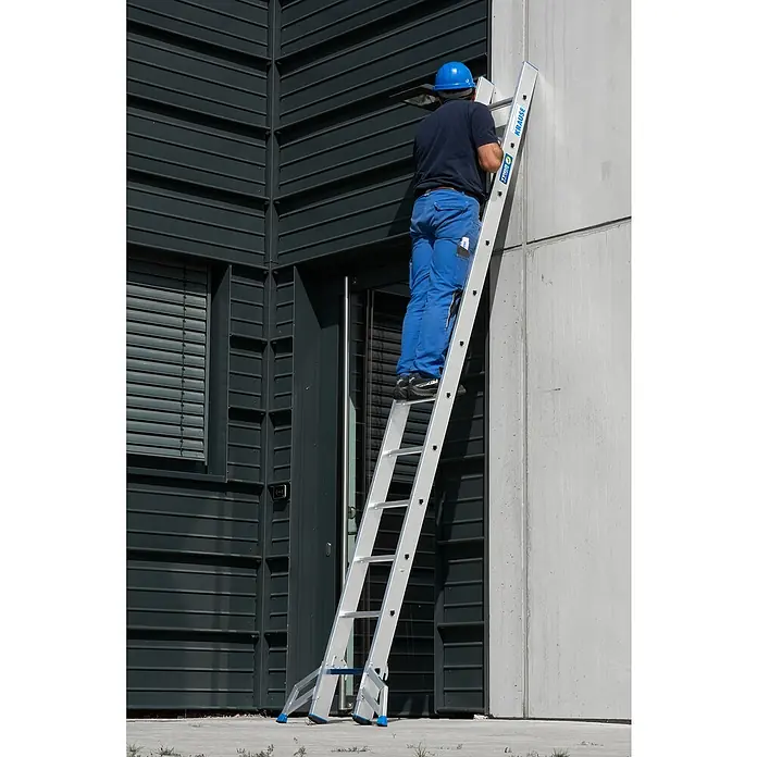 Krause Stabilo Schiebeleiter +S - Anzahl Tritte: 24 Stk., Arbeitshöhe: 6,7 m, Aluminium - Mann auf einer KRAUSE Leiter vor einem Gebäude. Die Leiter ist aus Aluminium und hat blaue Akzente. Er trägt Arbeitskleidung und einen blauen Helm.
