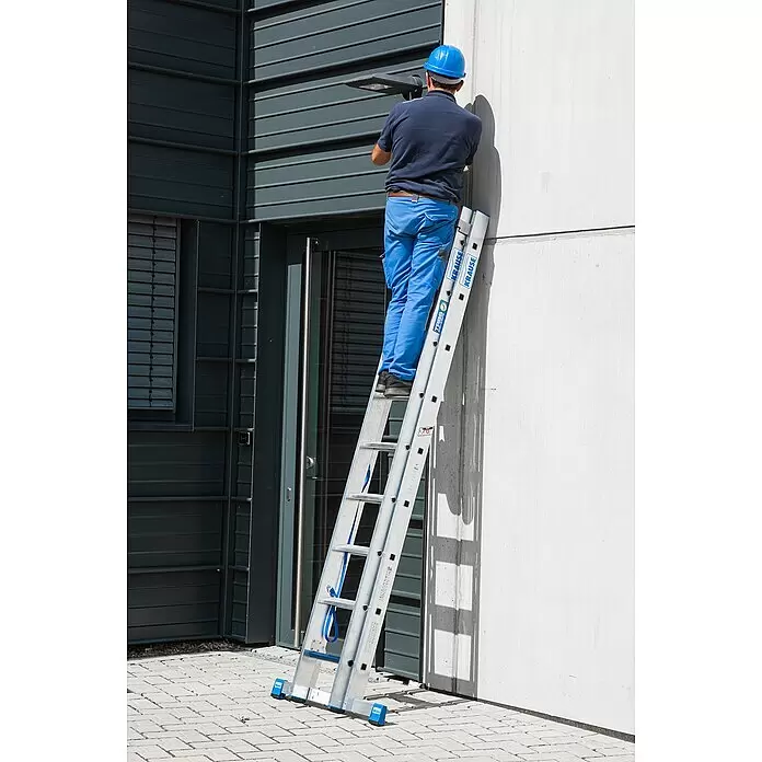 Krause Stabilo Mehrzweckleiter +S - Anzahl Tritte: 18 Stk., Arbeitshöhe: 5,15 m, Aluminium - Silberne und blaue Leiter, von einer Person verwendet, um einen hohen Punkt an einer Gebäudewand für Installationsarbeiten zu erreichen.