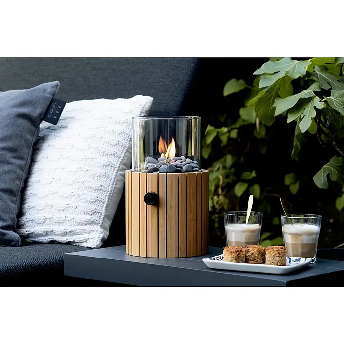 Gaslaterne Cosiscoop Timber - Holz, Ø x H: 18,5 x 30 cm, Rund - Nahaufnahme einer Cosi-Feuerstelle mit Getränken und Kuchen auf einem Tisch im Freien, die eine warme und einladende Atmosphäre schafft.