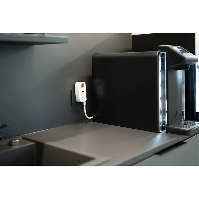 Überspannungsadapter - Weiß, Mit Schalter - Das Bild zeigt eine moderne Küche mit einem eleganten Wasserspender. Eine Steckdose mit Adapter ist an der Wand montiert.