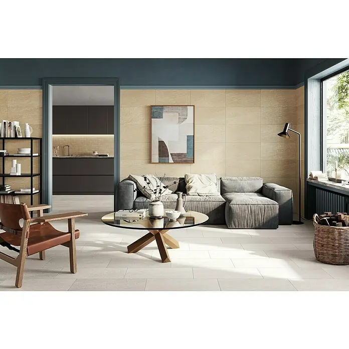 Atlas Concorde Solution Lane Feinsteinzeugfliese - 30 x 60 cm, Pearl, Matt - Wohnzimmer mit beigen Wandfliesen, grauer Couch und Holzakzenten für ein modernes, gemütliches Ambiente. Elegante Gestaltung mit Bücherregal und Fenstern.
