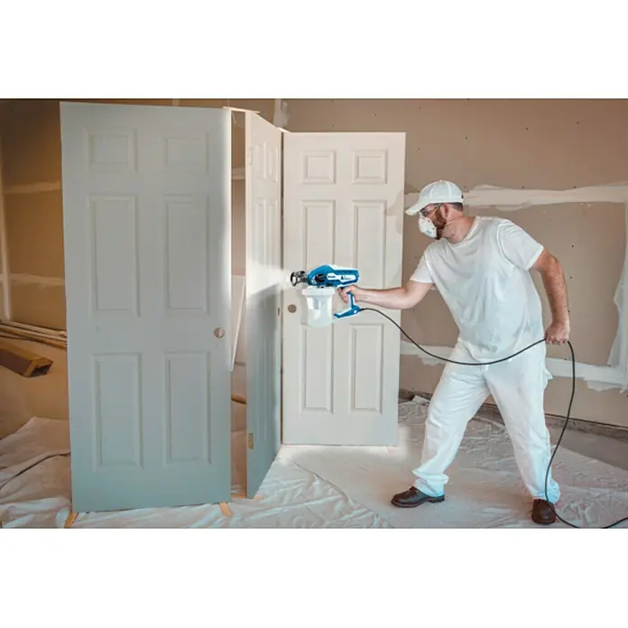 Graco Magnum Sistema de pulverización de pintura Compact A5DS - Velocidad de trabajo: 6 m²/min - Un hombre está usando un pulverizador de pintura para pintar puertas. El pulverizador Wagner asegura una aplicación uniforme de la pintura.