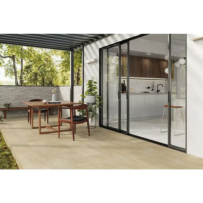 Atlas Concorde Solution Lane Feinsteinzeugfliese - 30 x 60 cm, Desert, Matt - Ein Terrassenbereich mit sandfarbenen Fliesen, einem Holztisch und Stühlen, der durch Schiebetüren in eine moderne Küche übergeht.