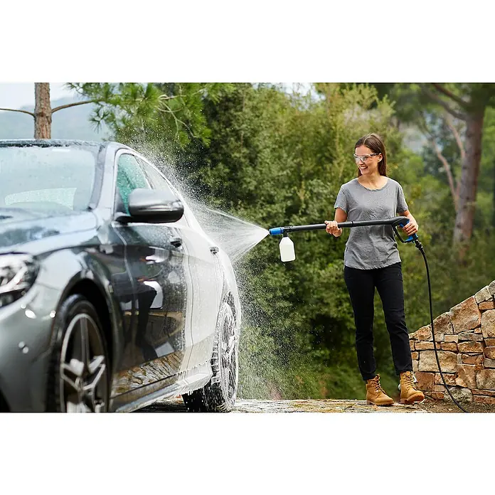 Nilfisk Kit de limpieza de automóviles - 3 pzs. - Una mujer usa una hidrolavadora para lavar un coche. La hidrolavadora rocía espuma en el lateral del coche.