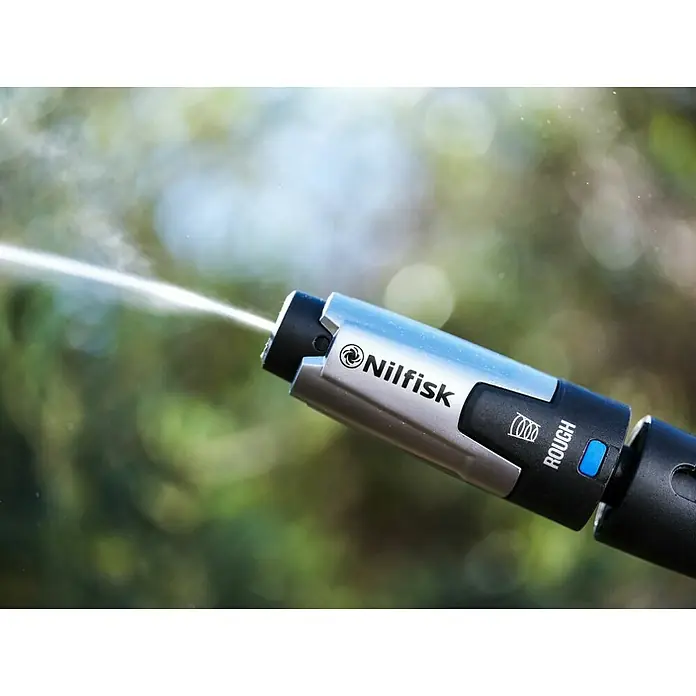 Nilfisk Boquilla de alta presión Premium Rough - Específico para: Hidrolimpiadoras Nilfisk Premium 180, 190 y 200 - Boquilla de hidrolimpiadora Nilfisk en acción, cuerpo plateado con punta negra y botón azul, rociando agua sobre un fondo verde.