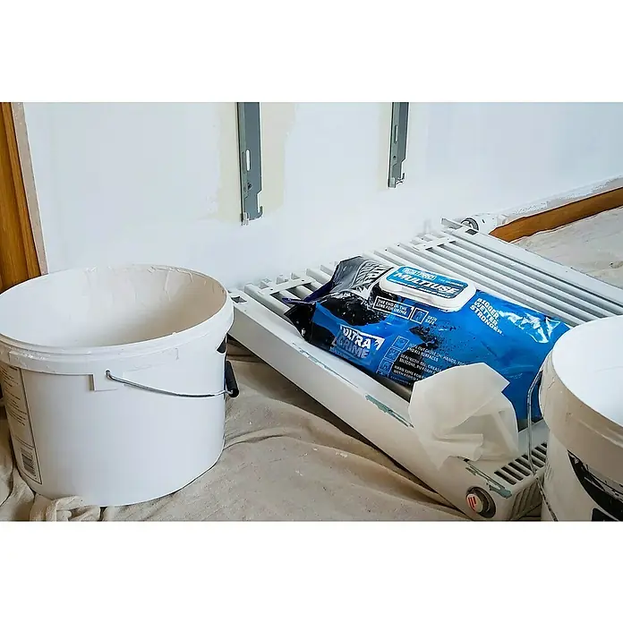 Feuchte Reinigungstücher Ultra Grime - 100 Stk. - Farbeimer und Ultra Grime Wischtücher liegen auf einem Heizkörper während Renovierungsarbeiten, die für eine schnelle Reinigung und effizientes Arbeiten sorgen.
