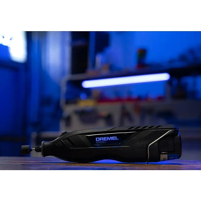 Dremel Herramienta rotativa a batería 8260 - 12 V, 3 Ah, Número de revoluciones de marcha en vacío: 5.000 r.p.m. - 30.000 r.p.m. - Primer plano de una herramienta rotativa inalámbrica Dremel 8260 sobre un banco de trabajo con iluminación azul al fondo.