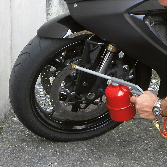 Herkules Pro-Line Flüsterkompressor TB 50V - 1.100 W, 50 l - Nahaufnahme des Reinigungsvorgangs eines Motorrads mit einer roten Reinigungsflüssigkeit, die auf die Bremsscheibe gesprüht wird.