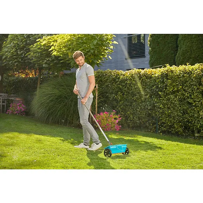 Gardena Combisystem Streuwagen - Streubreite: 40 cm, 3 l - Ein Mann benutzt einen GARDENA Streuwagen, um Dünger auf seinem Rasen zu verteilen, wobei er eine gleichmäßige Verteilung erzielt.