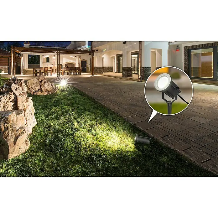Lavida Milan LED-Strahler - 8 W, 1.200 lm, 4.000 K, L x B x H: 31,6 x 15,5 x 11,5 cm, IP65, Rund - Beleuchteter Gartenbereich mit einem fokussierten Bodenspot, der Licht auf Rasen und Steine wirft. Detailaufnahme eines Strahlers hervorgehoben.