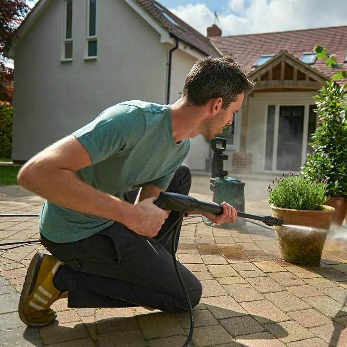 Bosch Hochdruckreiniger UniversalAquatak 125 - 125 bar, 1.500 W, Fördermenge: 360 l/h - Ein Mann kniet und reinigt einen Blumentopf mit einem Hochdruckreiniger im Garten.