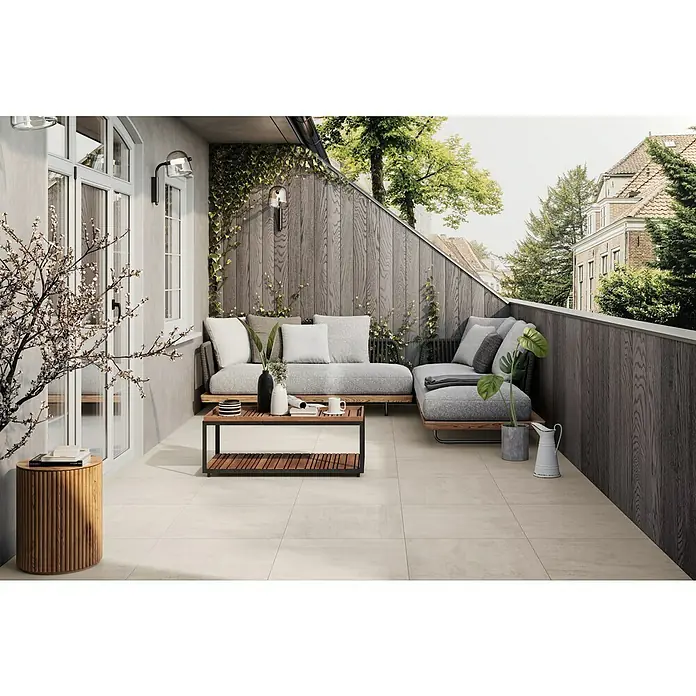 Atlas Concorde Solution Terrassenfliese Rover Ivory - 60 x 60 x 2 cm, Beige, Matt - Ein stilvoller Außenbereich mit beigen Bodenfliesen, einer grauen Couch und Holzelementen. Ideal für entspannte Stunden im Freien mit modernem Flair.