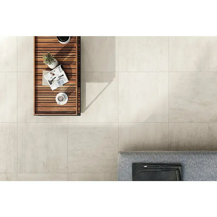 Atlas Concorde Solution Terrassenfliese Rover Ivory - 60 x 60 x 2 cm, Beige, Matt - Ein heller Raum mit großformatigen Bodenfliesen in neutralen Tönen und einem Holztisch mit Accessoires für einen modernen Look.