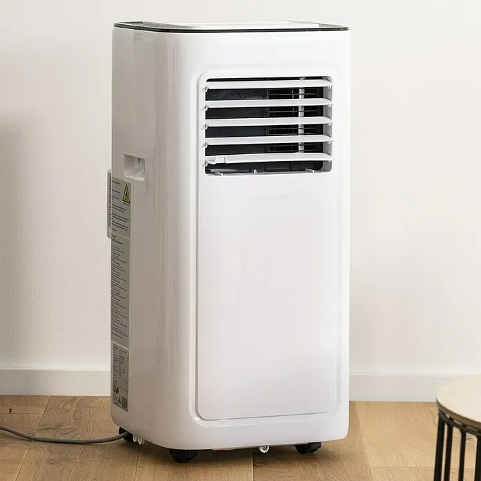 Voltomat Aire acondicionado portátil Boreas - 2.000 W, Tamaño de la estancia: 20 m², Blanco/Negro - Un aparato de aire acondicionado portátil blanco se apoya en un piso de madera, con ventilaciones frontales y ruedas para facilitar el movimiento.