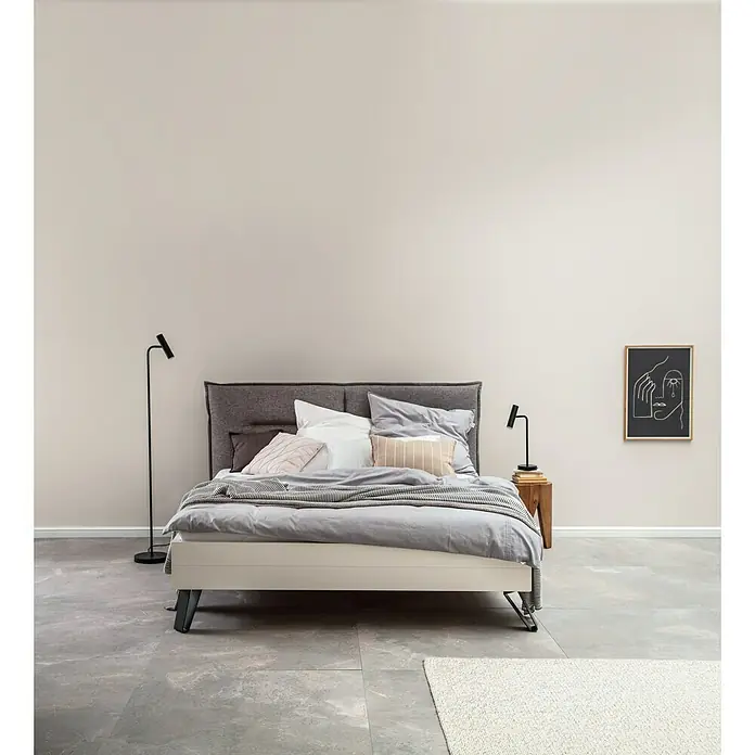 SCHÖNER WOHNEN-Farbe Wandfarbe Trendfarbe - Cosy, Matt, 5 l, Konservierungsmittelfrei - Ein stilvolles Bett mit einem grauen Kopfteil, weichen Kissen und einer gestreiften Decke, das Komfort und moderne Eleganz vereint.\n
