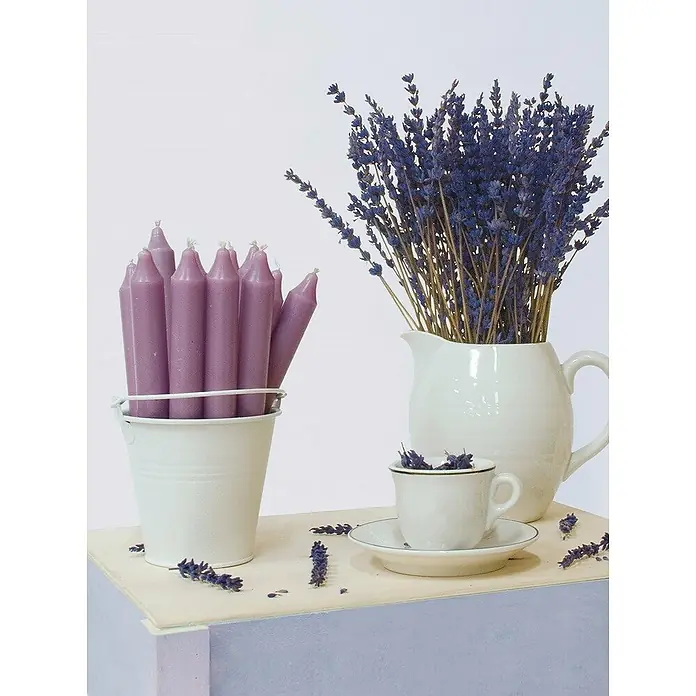 Ceras Roura Vaso con vela - Ø x Al: 7 x 8,5 cm, Lavanda - Naturaleza muerta con velas cónicas moradas en un cubo, lavanda en una jarra y una taza de té en una mesa.