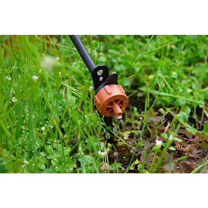 Gotero lineal autocompensado marrón - Diámetro: 4 mm, 25 ud. - Primer plano de un gotero de riego marrón con una gota de agua en una varilla negra, enclavado en una exuberante vegetación.